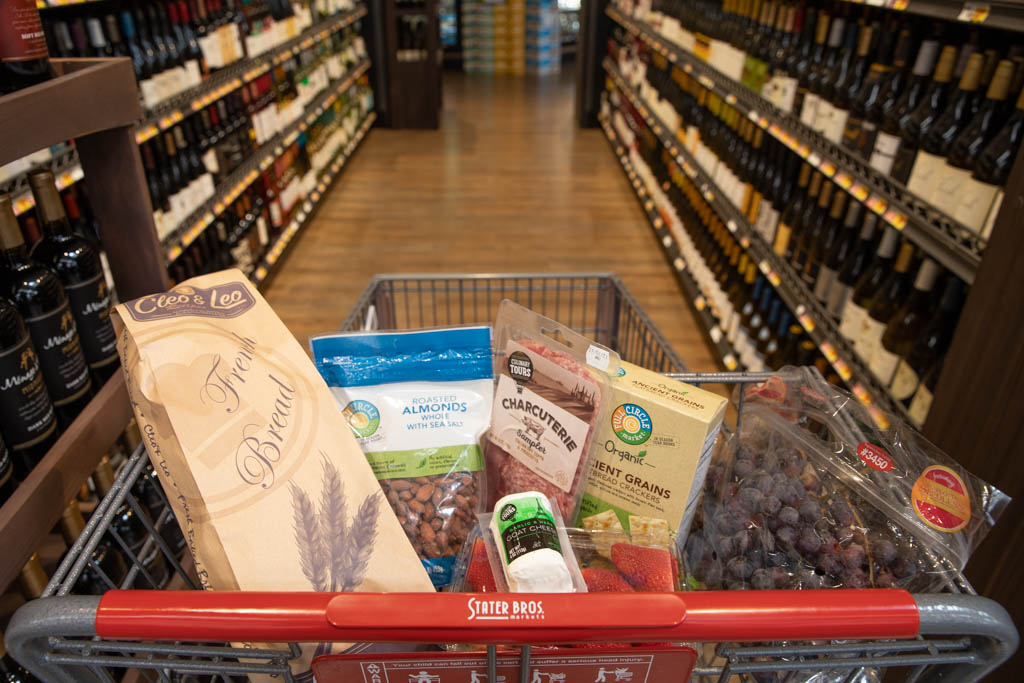 Grocery cart with groceries in wine aisle.