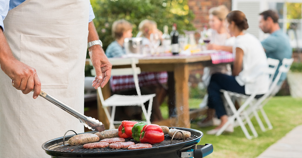 Man barbequing with family in background.