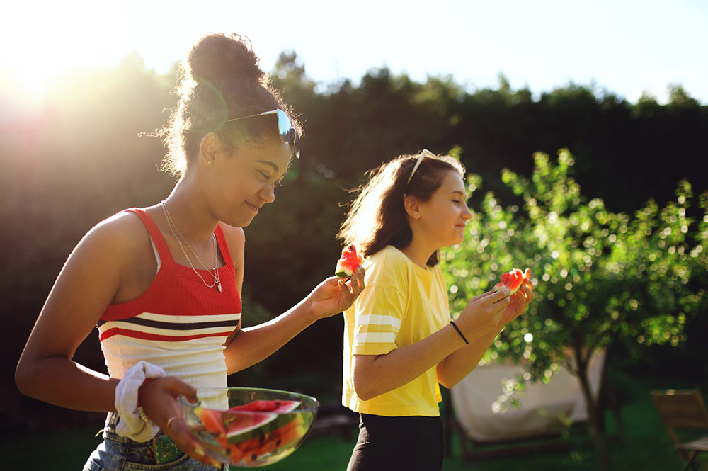 Teenagers eating watermelon outdoors.