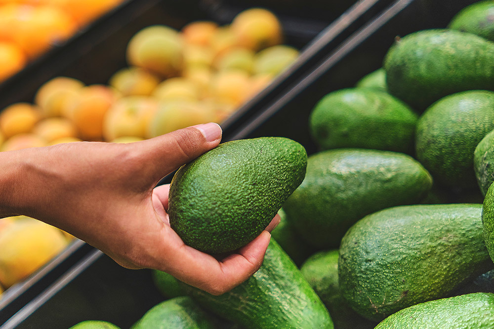 Person picking avocado in grocery store.