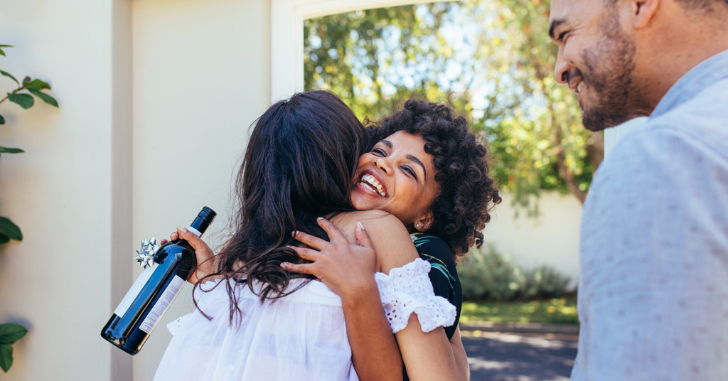 A friend giving a warm congratulatory hug and gifting a bottle of wine.