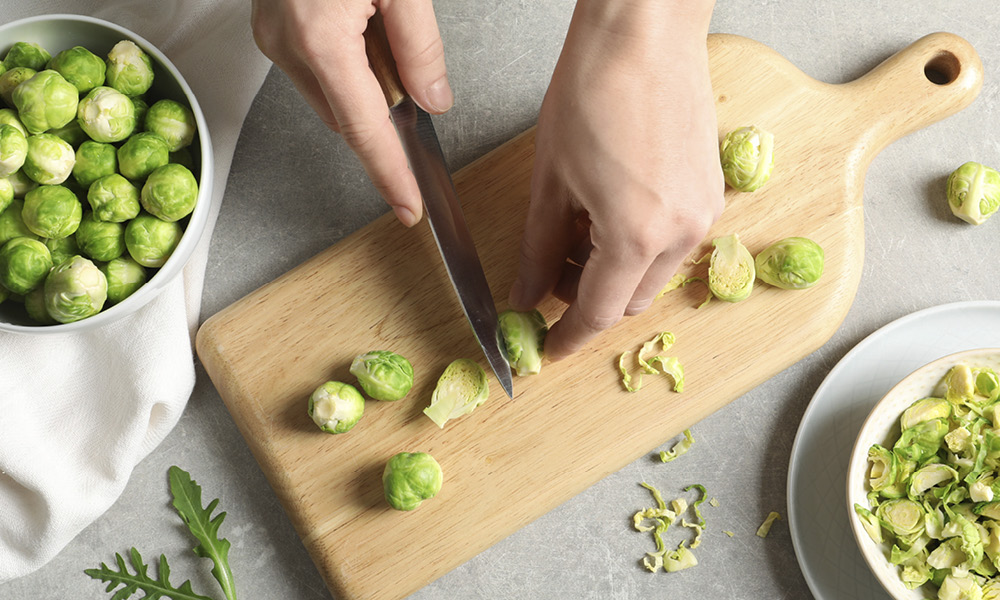 A person chopping the ends off of brussels sprouts on a cutting board.