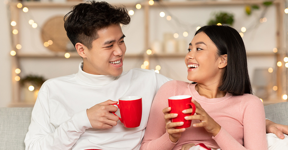 Young couple sitting down with hot chocolate and enjoying each other's company in a Christmas setting.