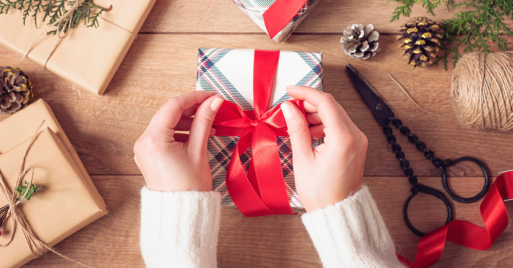 Two hands wrapping a small holiday gift box with a bow. 