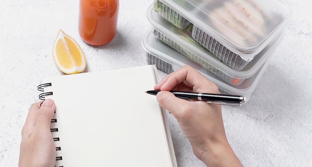 Young person writing out health goals on a notepad in the kitchen.