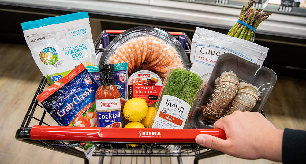 Hand pushing Stater Bros. Markets cart filled with different seafood selections.