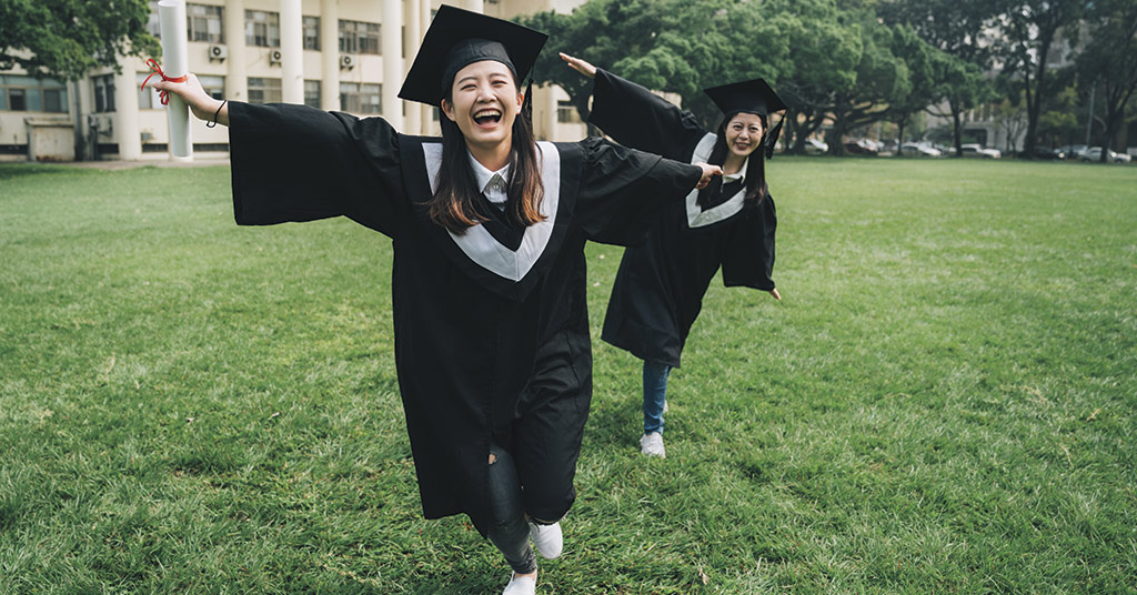 Two graduates running in courtyard celebrating.