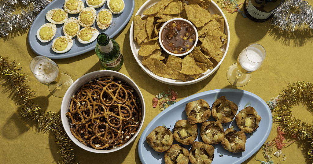 Table Setting With New Years Eve Appetizers Including Pretzels, Puff Pastries, Chips & Salsa, Deviled Eggs, Champagne and Stella Beer