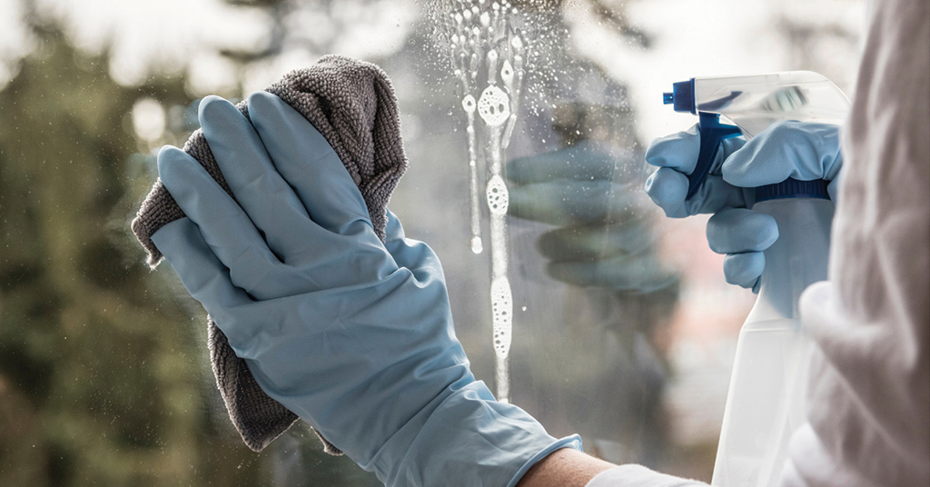 Person cleaning windows with a glass cleaner and microfiber cloth for spring cleaning.