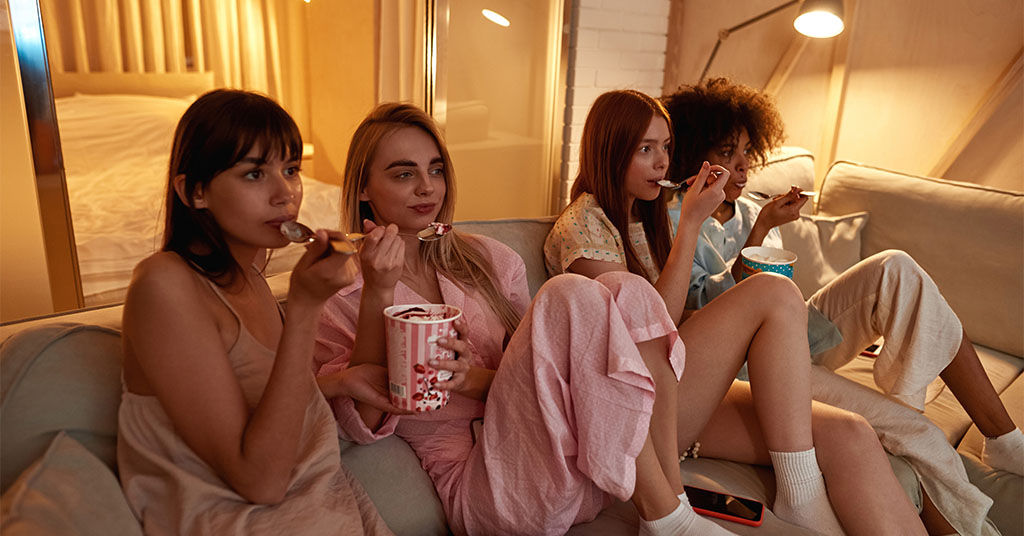 Gal friends getting together on Galentine's Day eating ice cream and watching a movie marathon.