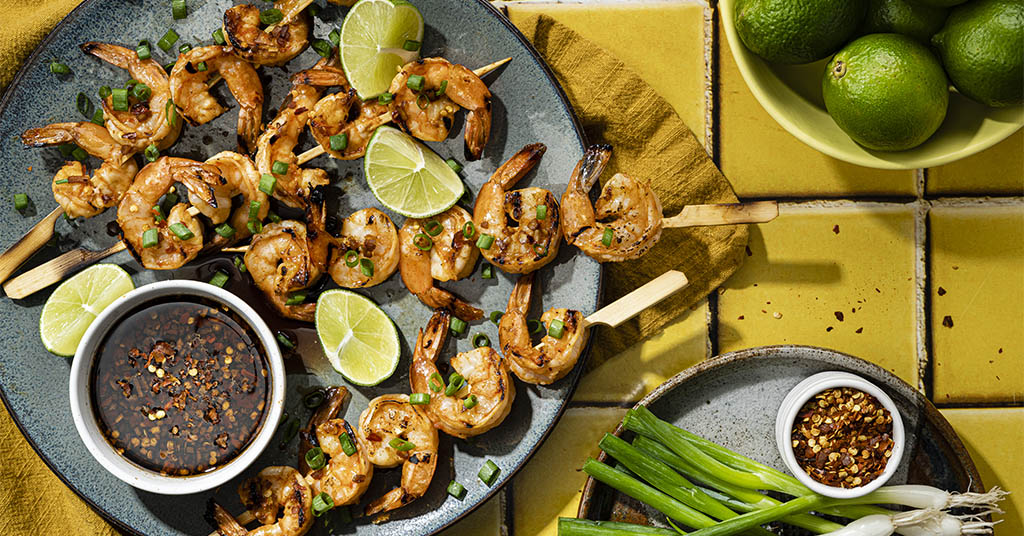 Shrimp skewers served with lime slices and a sweet chili dipping sauce.