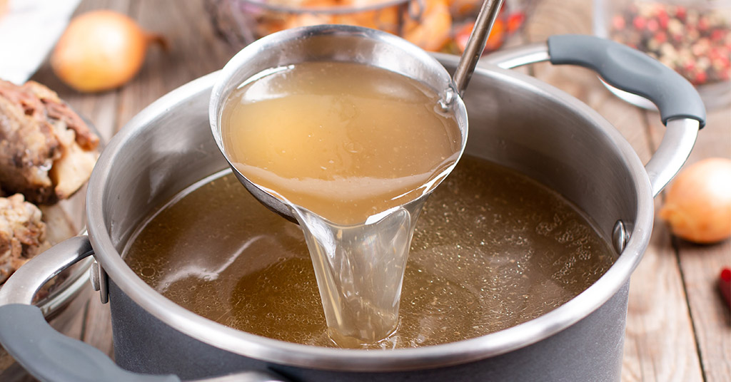 Saucepan with bouillon with a ladle on a wooden table. Bone broth