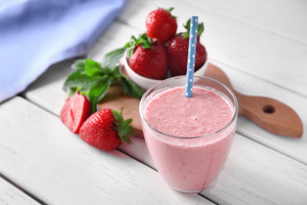 Glass cup filled with strawberry green tea smoothie with cut strawberries next to it, featured on Stater Bros. Markets